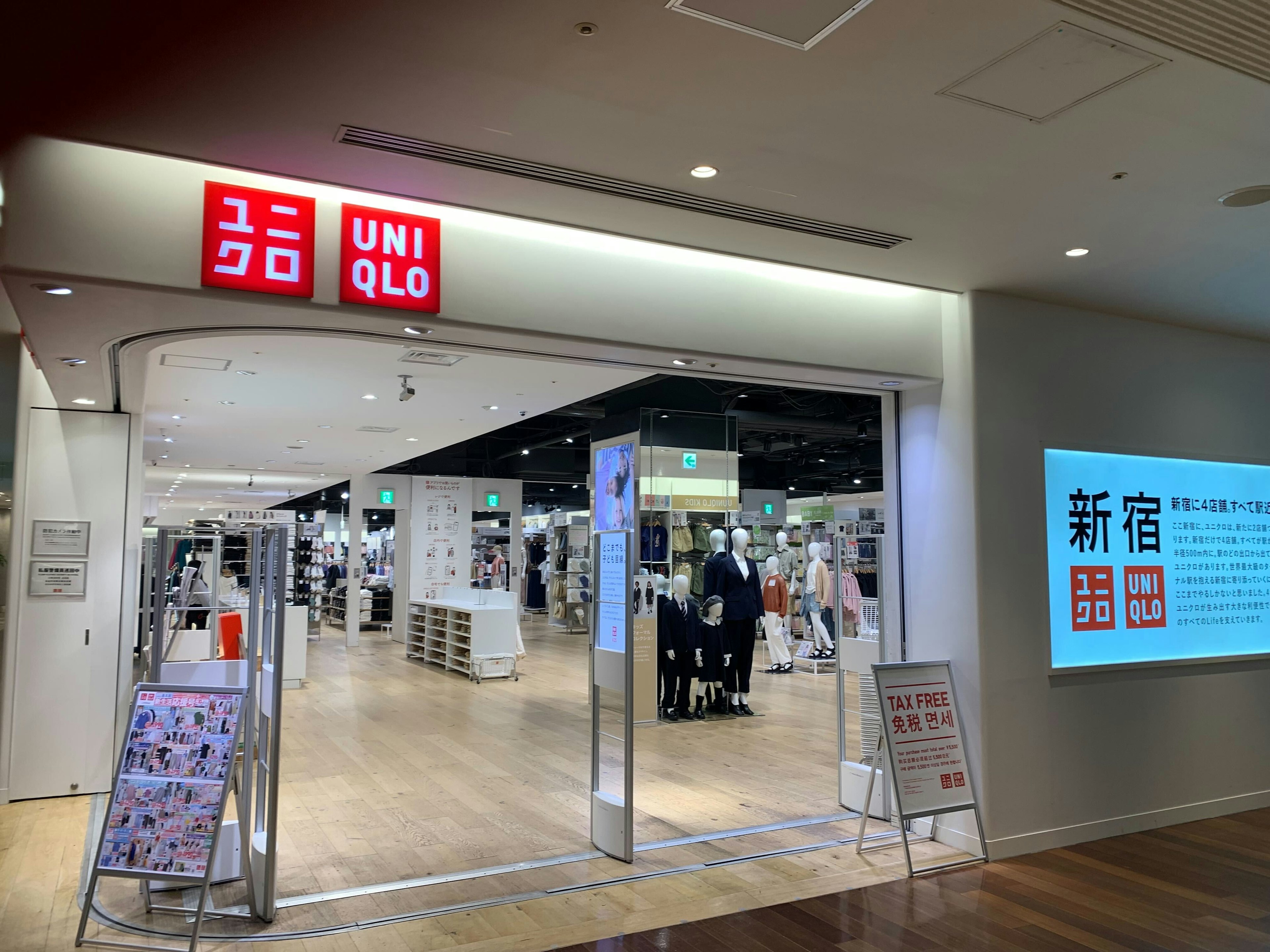 ユニクロ店舗の入り口。赤いロゴが目を引くアーチ型の入口の上に「UNIQLO」と表示されている。店内は明るく、広々としており、多様な衣料品が並んでいるのが見える。入り口には免税対象店舗であることを示す「TAX FREE SHOP」のサインも設置されている。