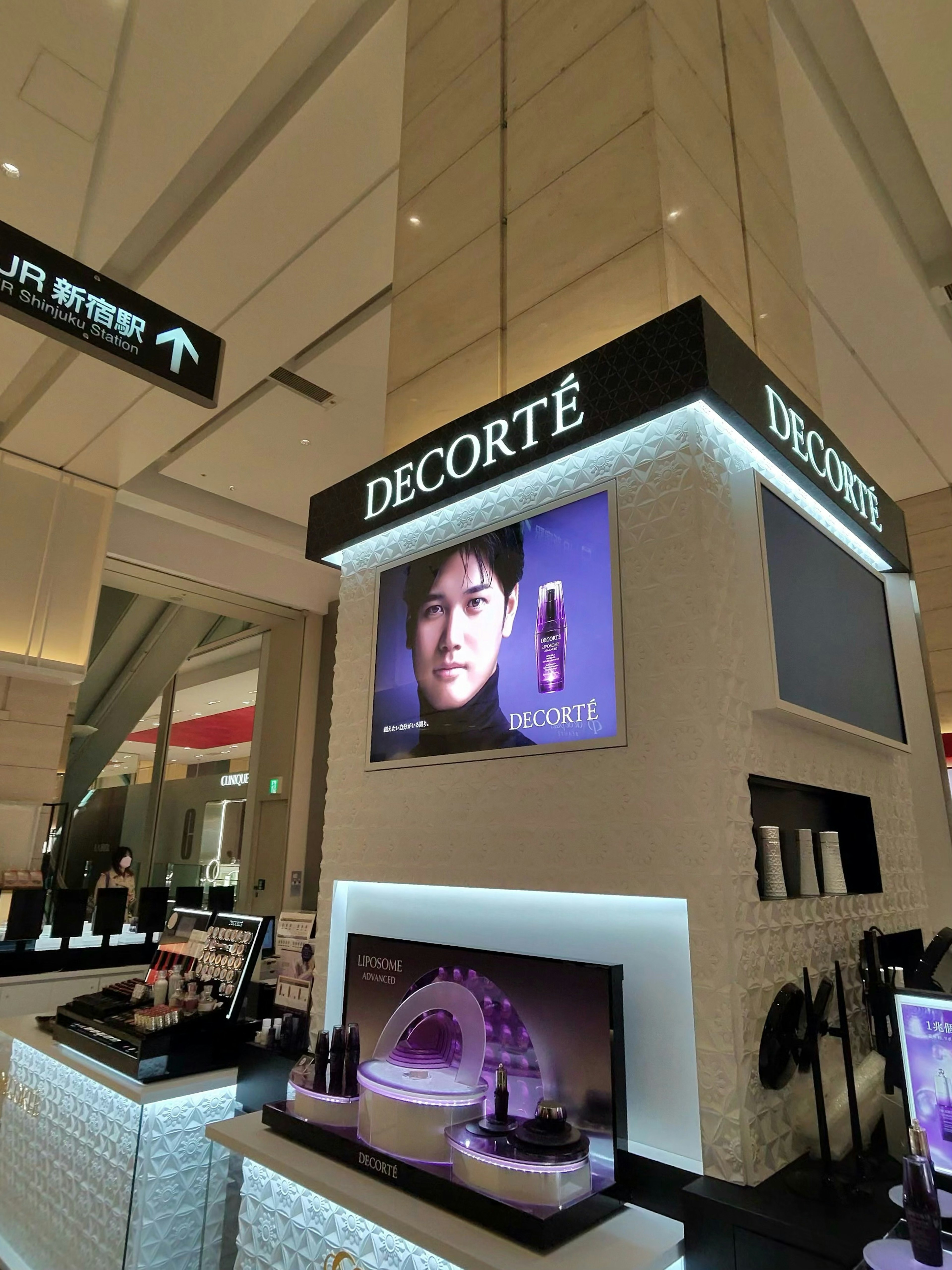 DECORTÉのコスメが展示されている店内の様子。背景には日本の男性モデルの顔が映し出された広告があり、DECORTÉのロゴが照明で照らされている
