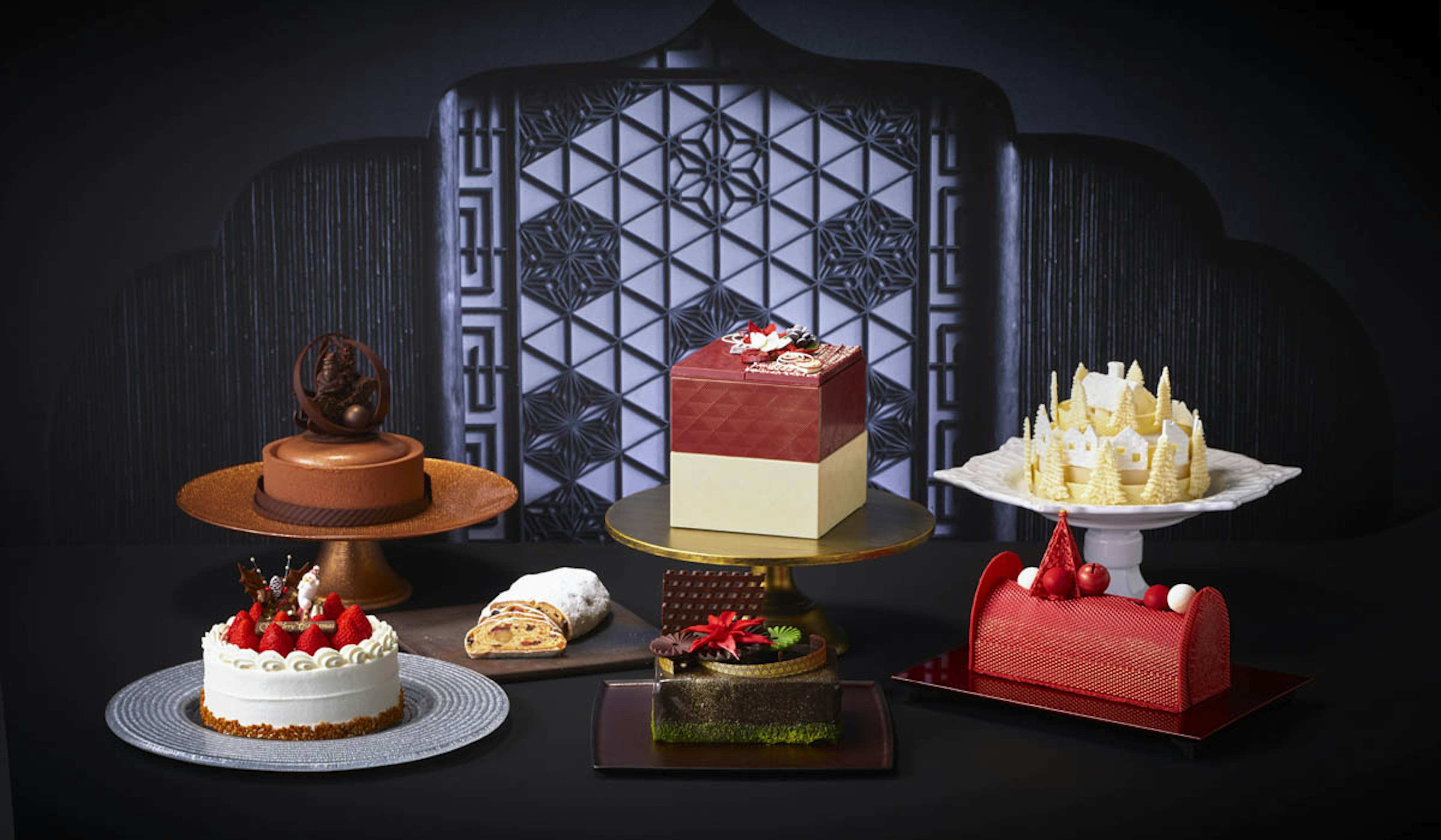 黒を基調とした背景にさまざまなデザインとカラーのクリスマスケーキが飾られている