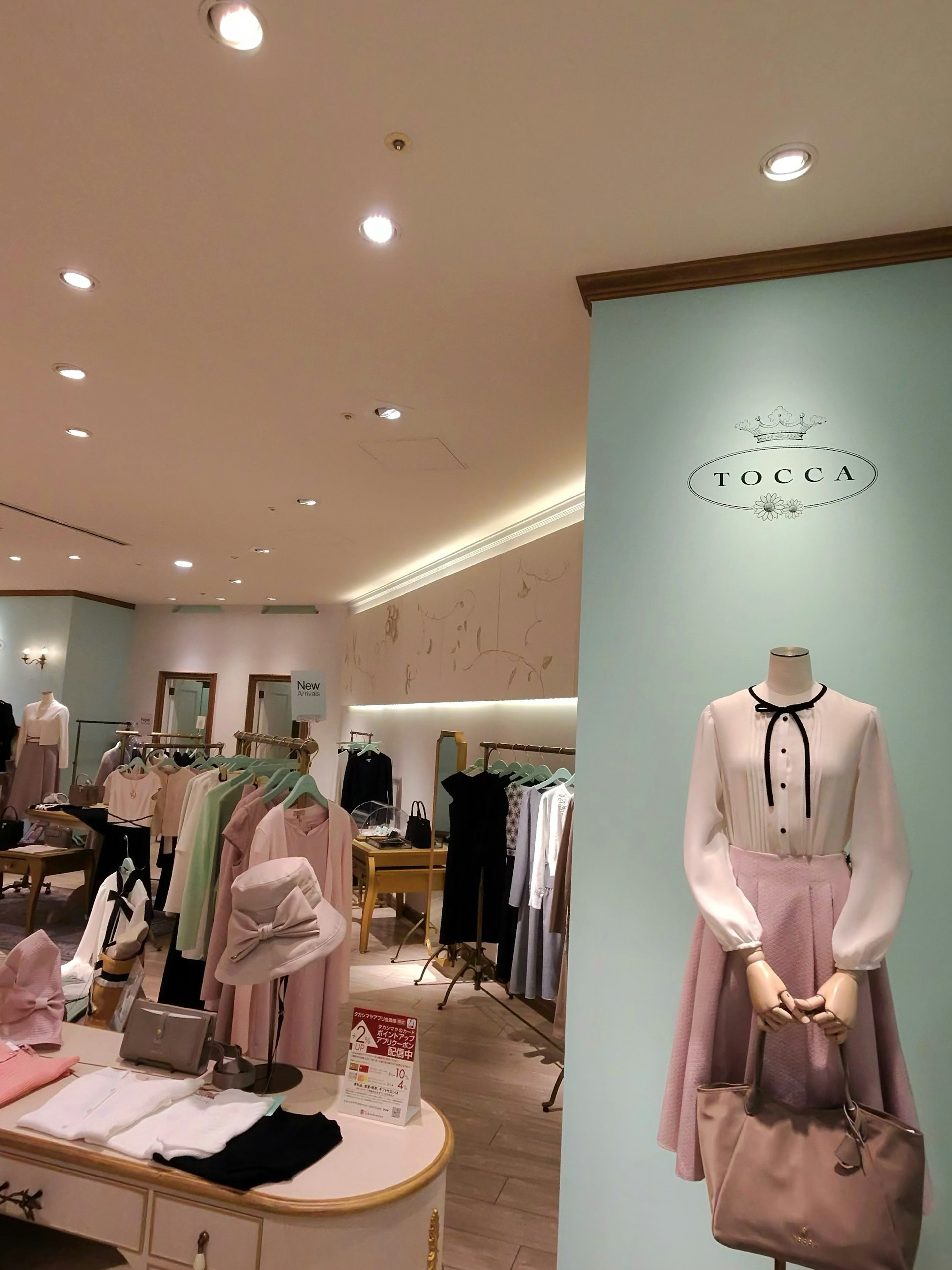 シックなインテリアのTOCCA店内。TOCCAのロゴが掲げられた壁の前にはエレガントなワンピースを着たマネキンがディスプレイされている