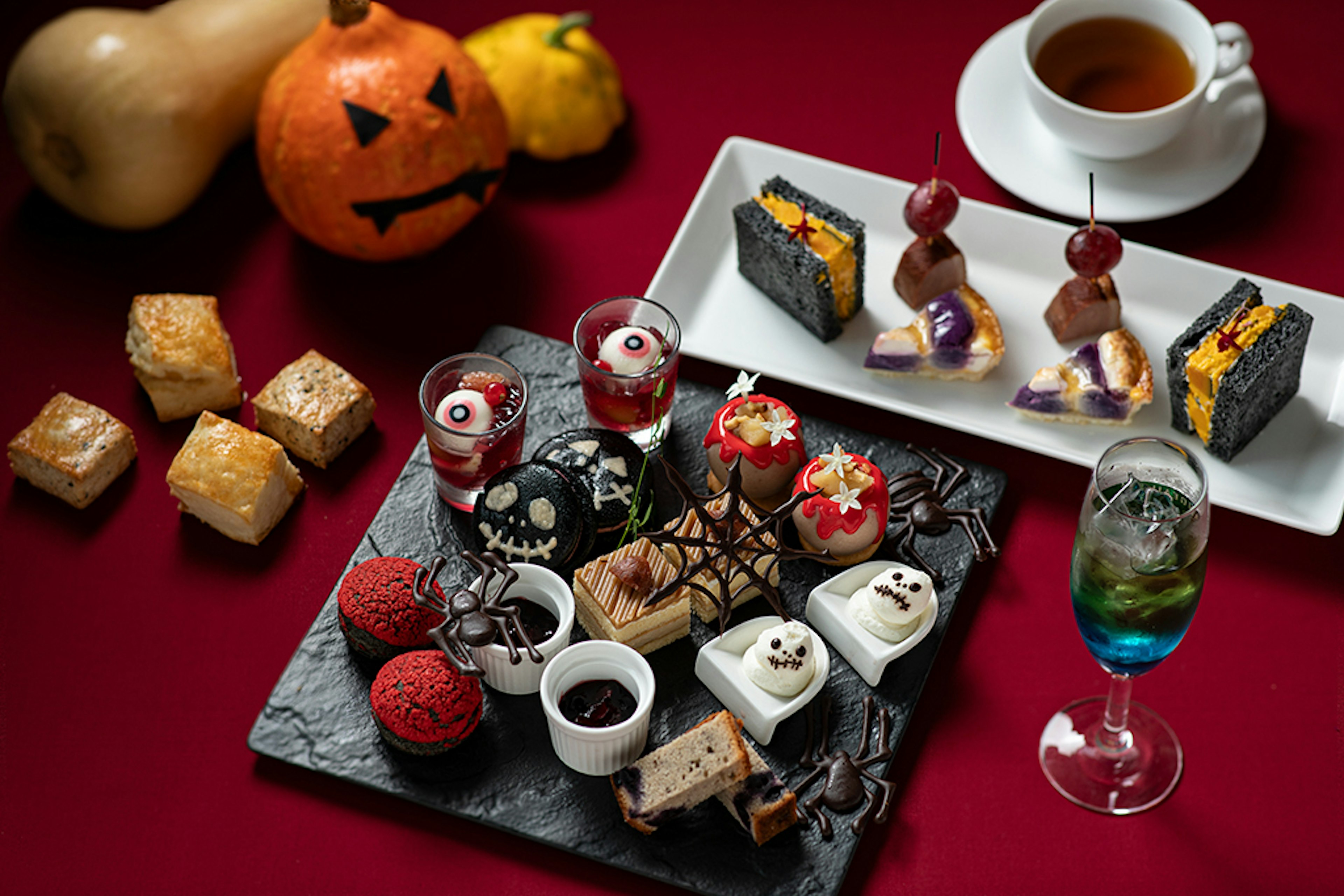 ハロウィンをテーマにしたスイーツと軽食のプレート。ジャックオランタンやクモの巣モチーフが可愛く、目玉や骸骨型のデザートも並んでいます。