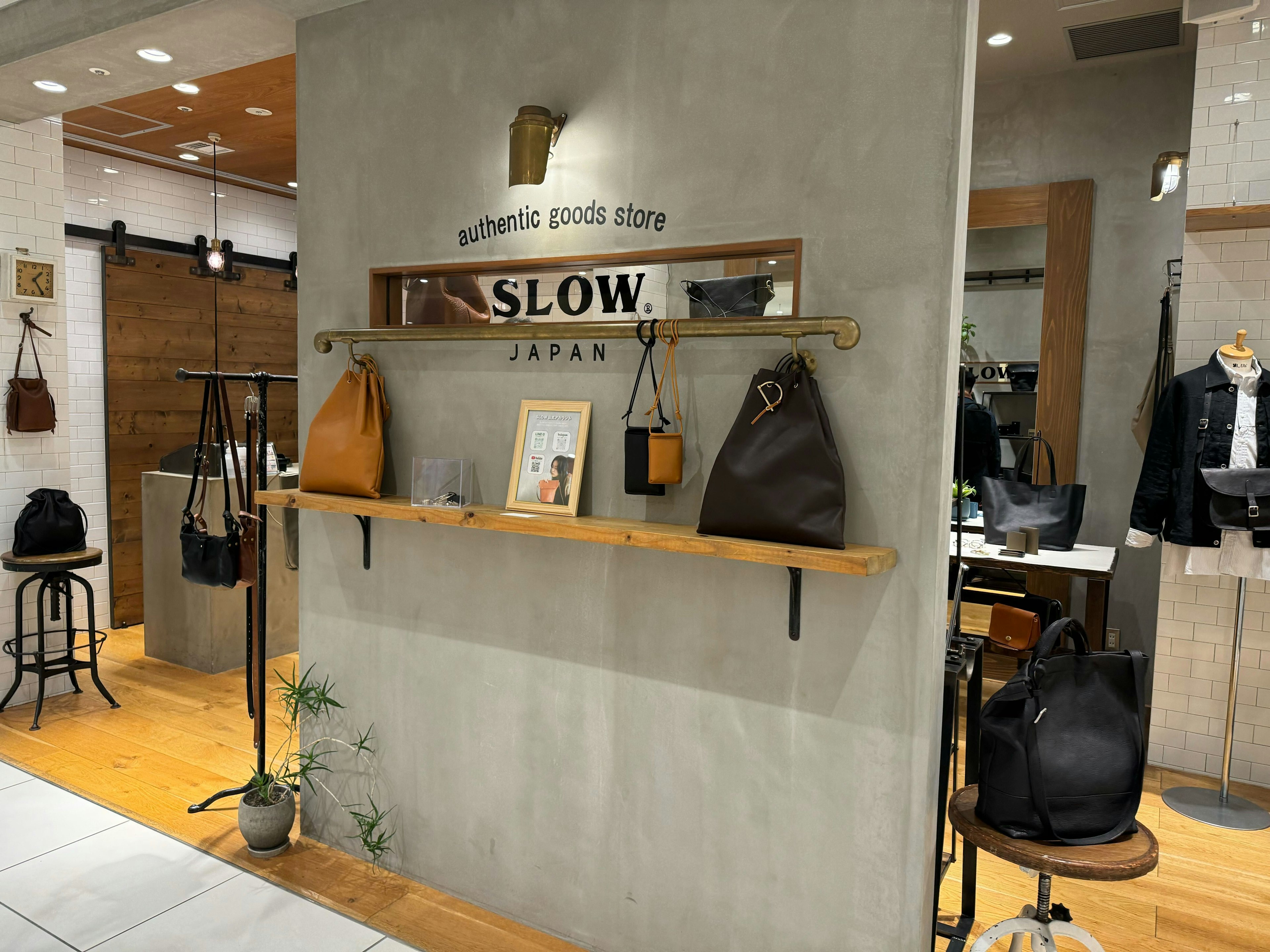 スロウ オーセンティック グッズ ストアの店内の全景。左側の壁面にはロゴがあり、手前にはレザーバッグが複数展示されています。