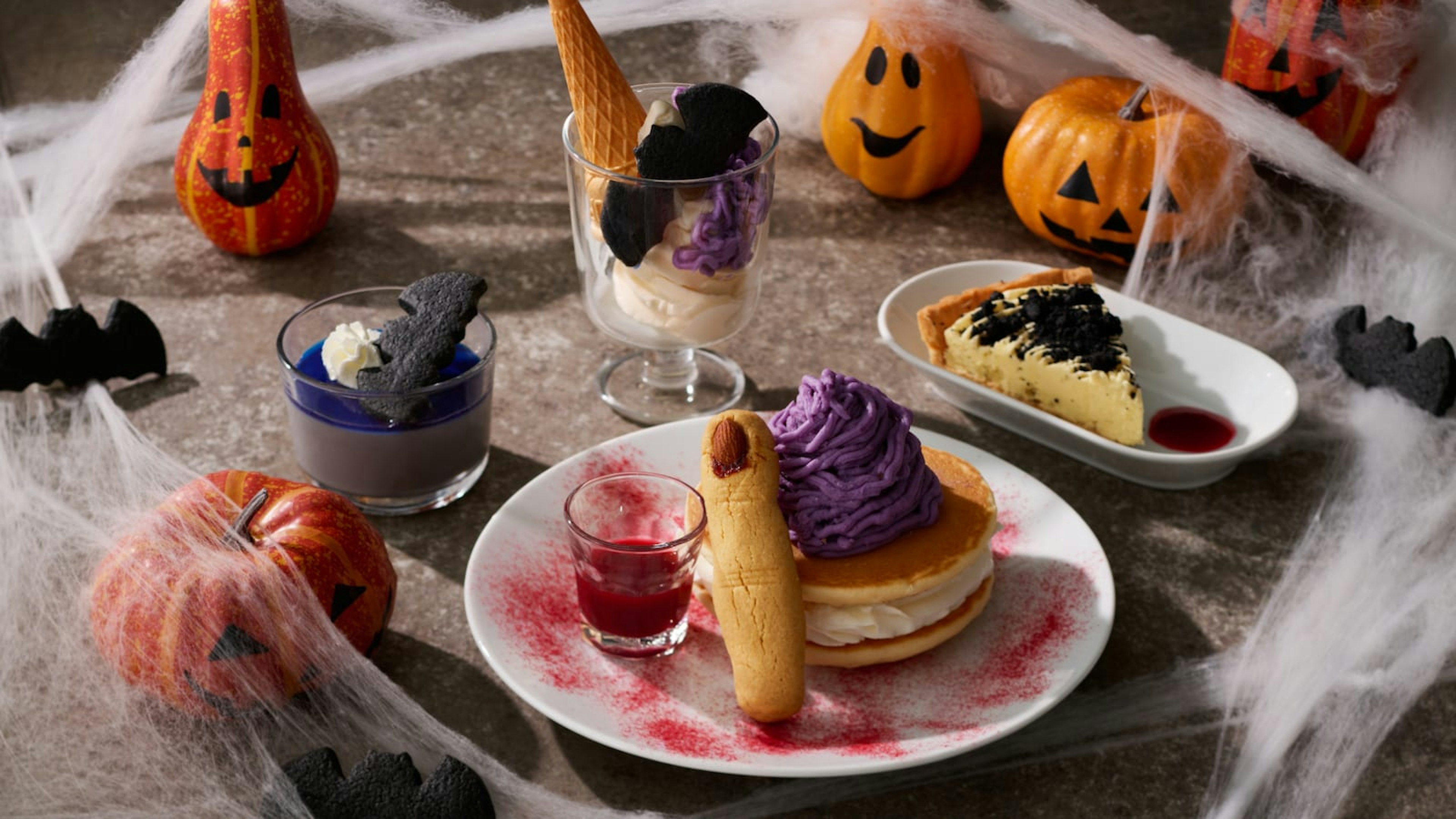 ハロウィンの装飾が施されたテーブルに、紫色のクリームやクッキーで飾られたデザートが並ぶスイーツプレート。