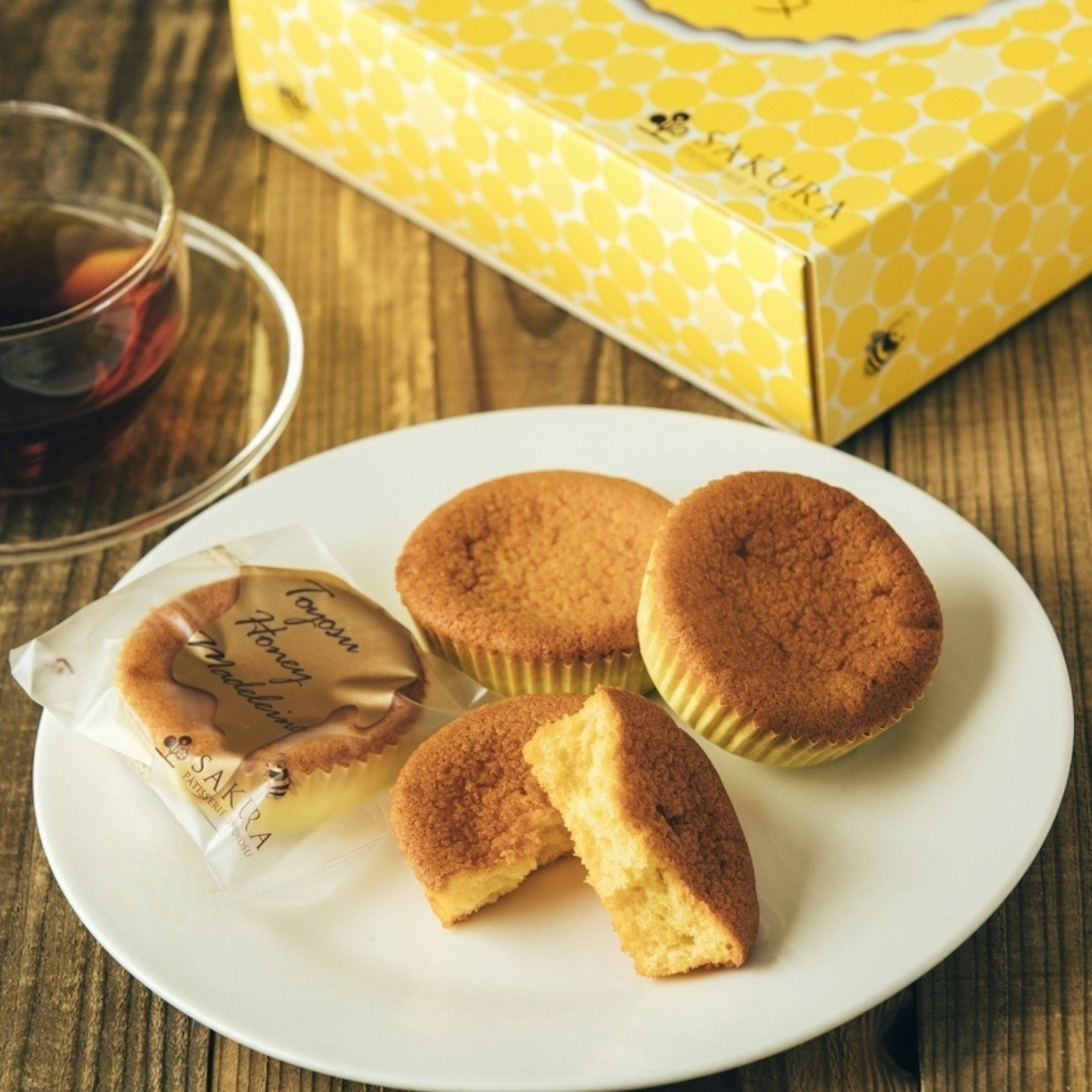 白い皿に盛られたはちみつ風味のマドレーヌと、黄色いパッケージが背景に見える。