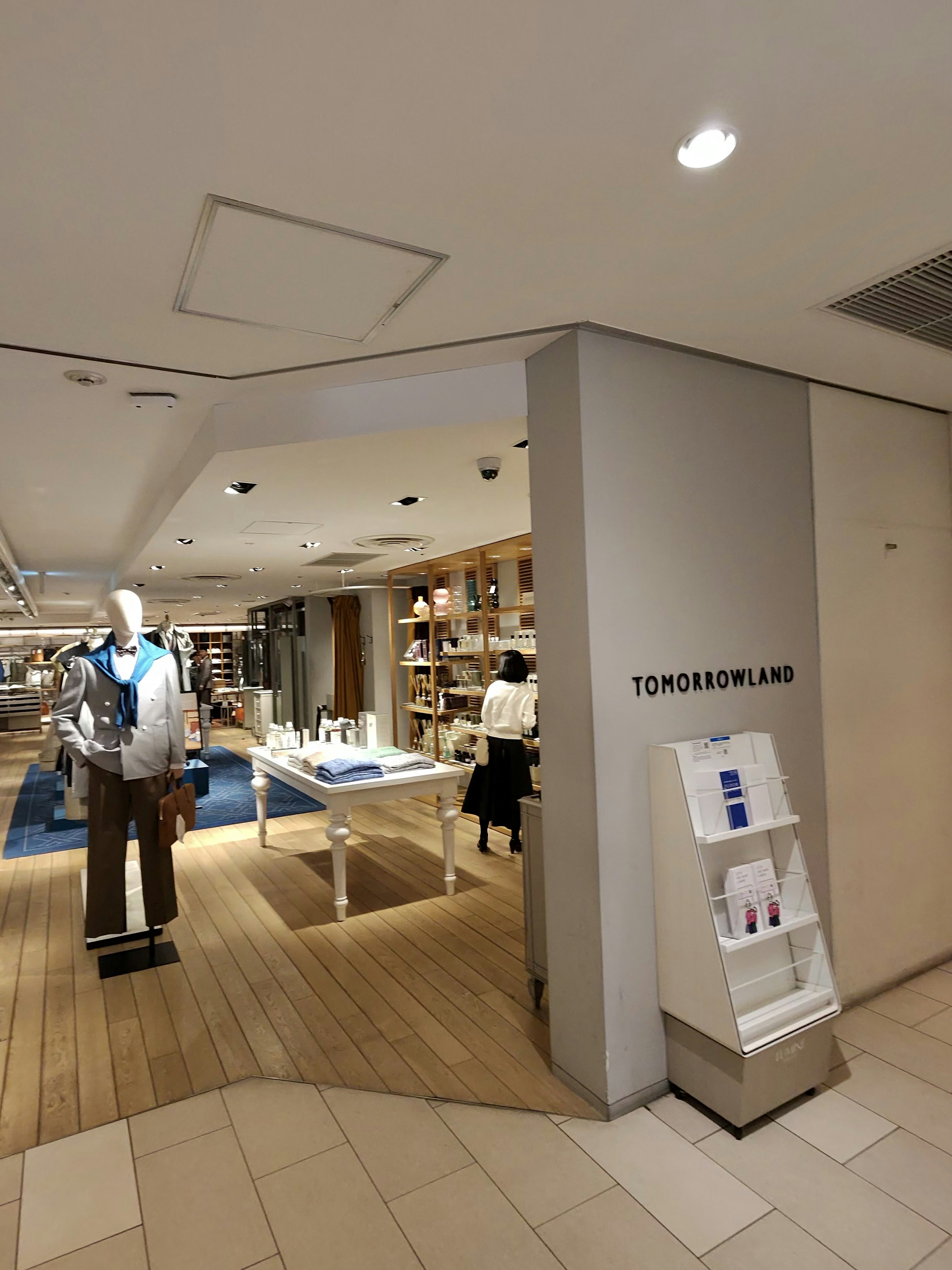 TOMORROWLANDブランドの入り口。店内は明るく、左側にはマネキンがグレーのジャケットを着て青いシャツを合わせて展示されています。