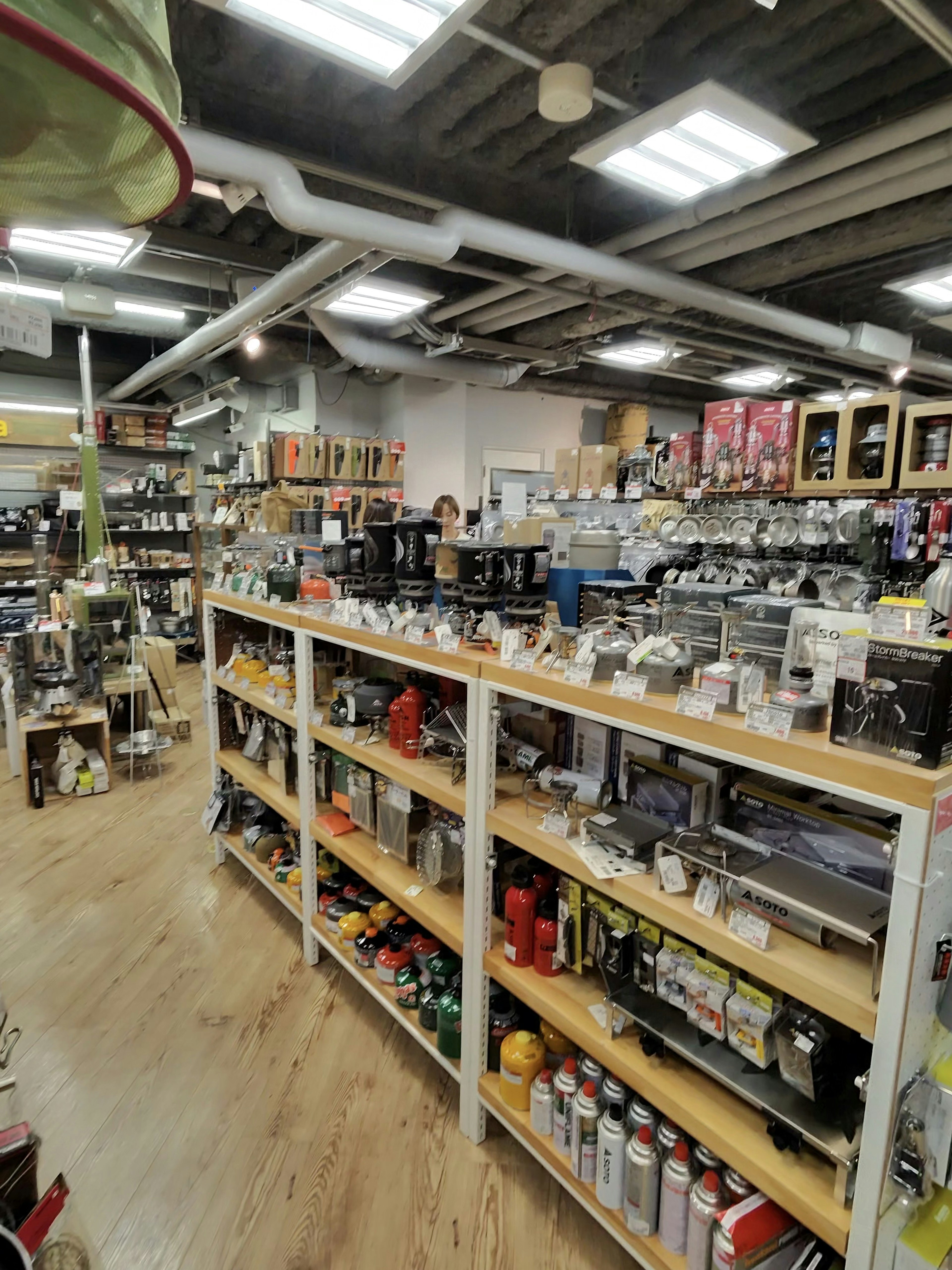 アウトドア用品店の店内。棚にはキャンプ用のガスボンベや調理器具が整然と並んでおり、広々とした売り場に豊富な商品がそろっている。